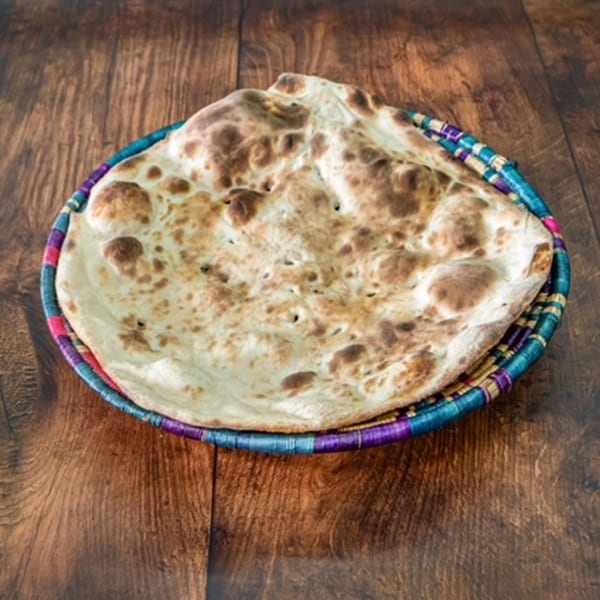 Freshly baked Yemeni bread, with a slightly charred top, served in a colorful woven basket.