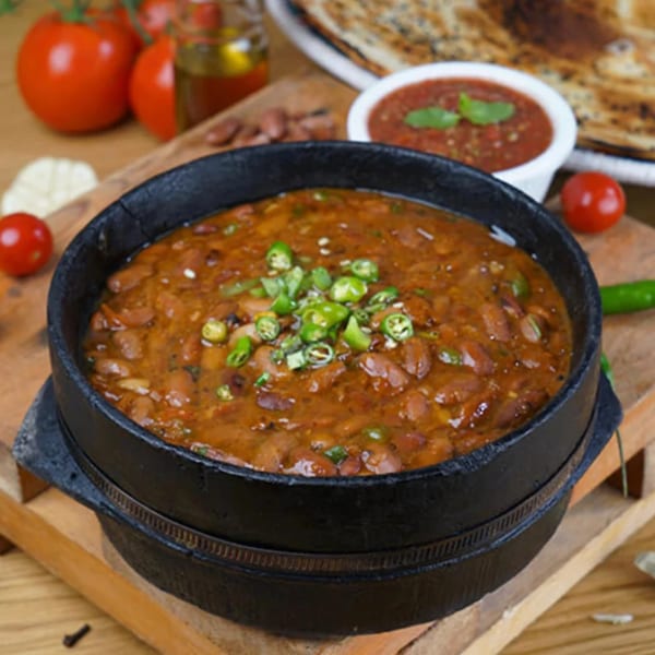 Foul Mudammas, a Yemeni fava bean stew, in a black pot with green chilies, tomatoes, and flatbread.