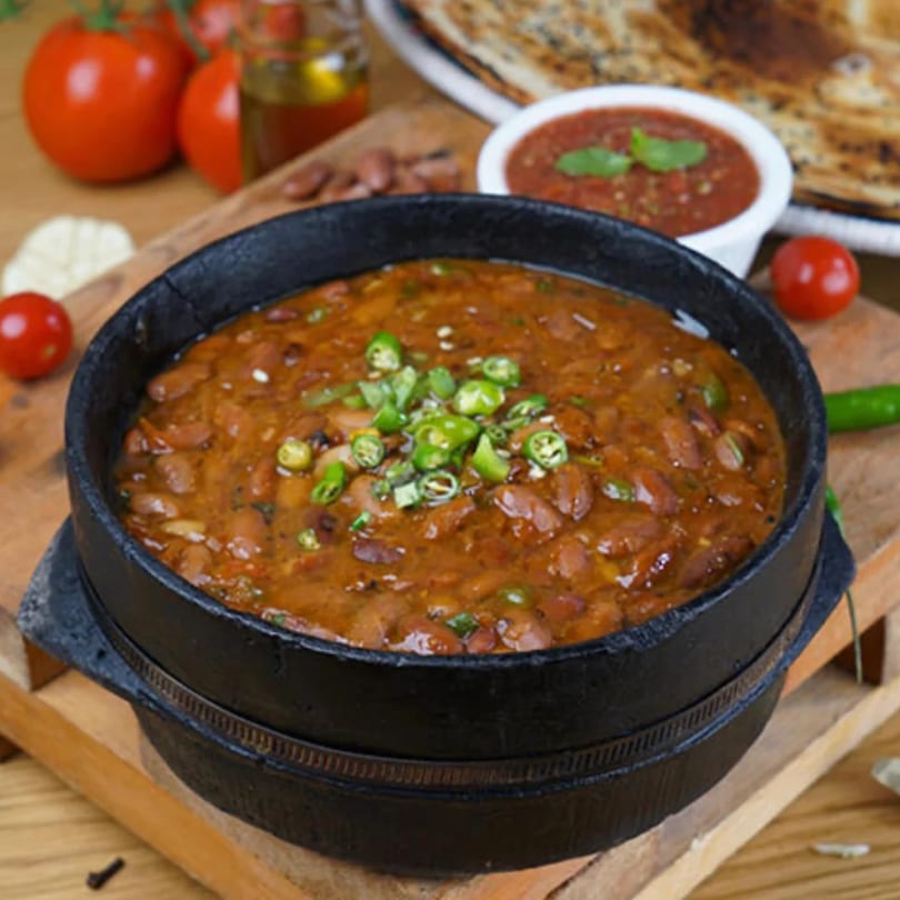 Foul Mudammas, a Yemeni fava bean stew, in a black pot with green chilies, tomatoes, and flatbread.