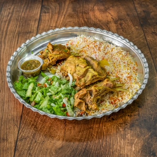 A large silver platter of Bab Al-Yemen's mandi lamb with rice, salad, and green sauce.