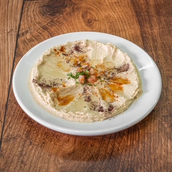 A white plate of creamy hummus, drizzled with olive oil and sprinkled with spices and parsley.