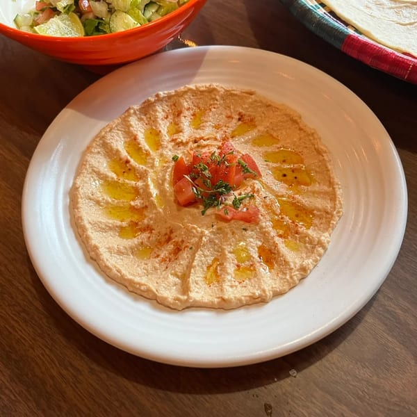 Creamy hummus drizzled with olive oil, topped with diced tomatoes and parsley, served on a white plate.