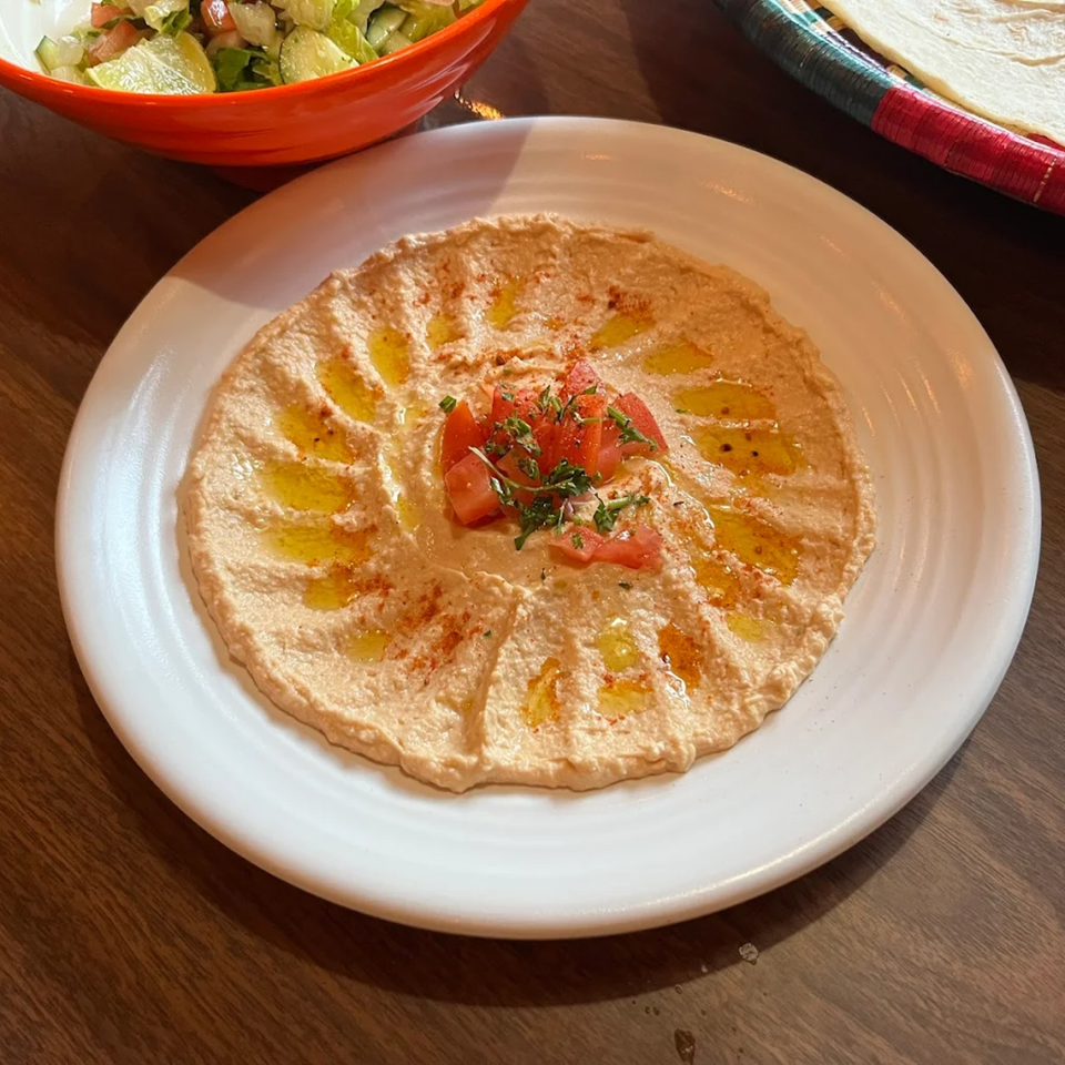 Creamy hummus drizzled with olive oil, topped with diced tomatoes and parsley, served on a white plate.